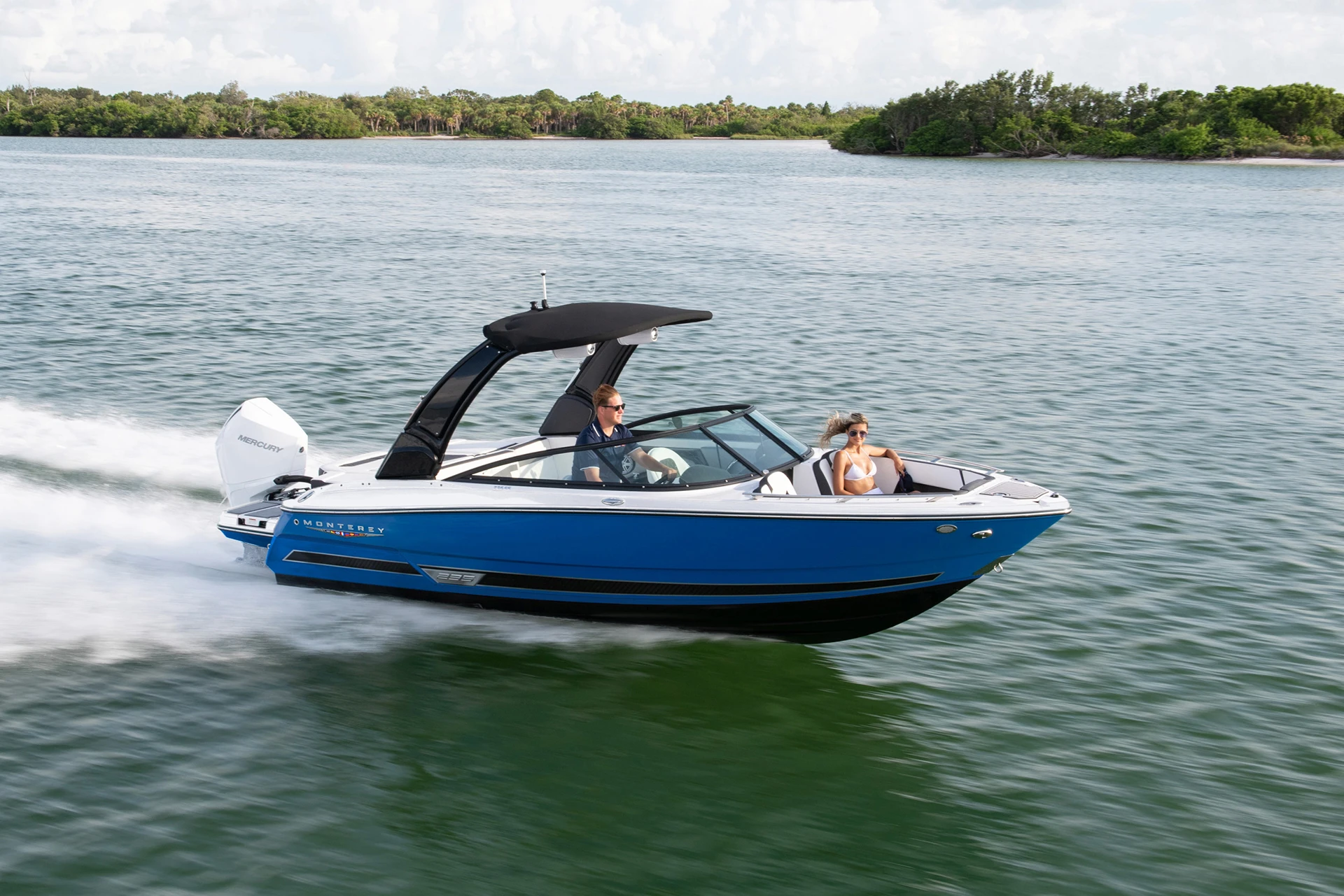 Monterey 235SS outboard bowrider cruising at speed with two passengers, featuring a blue hull and black wakeboard tower.