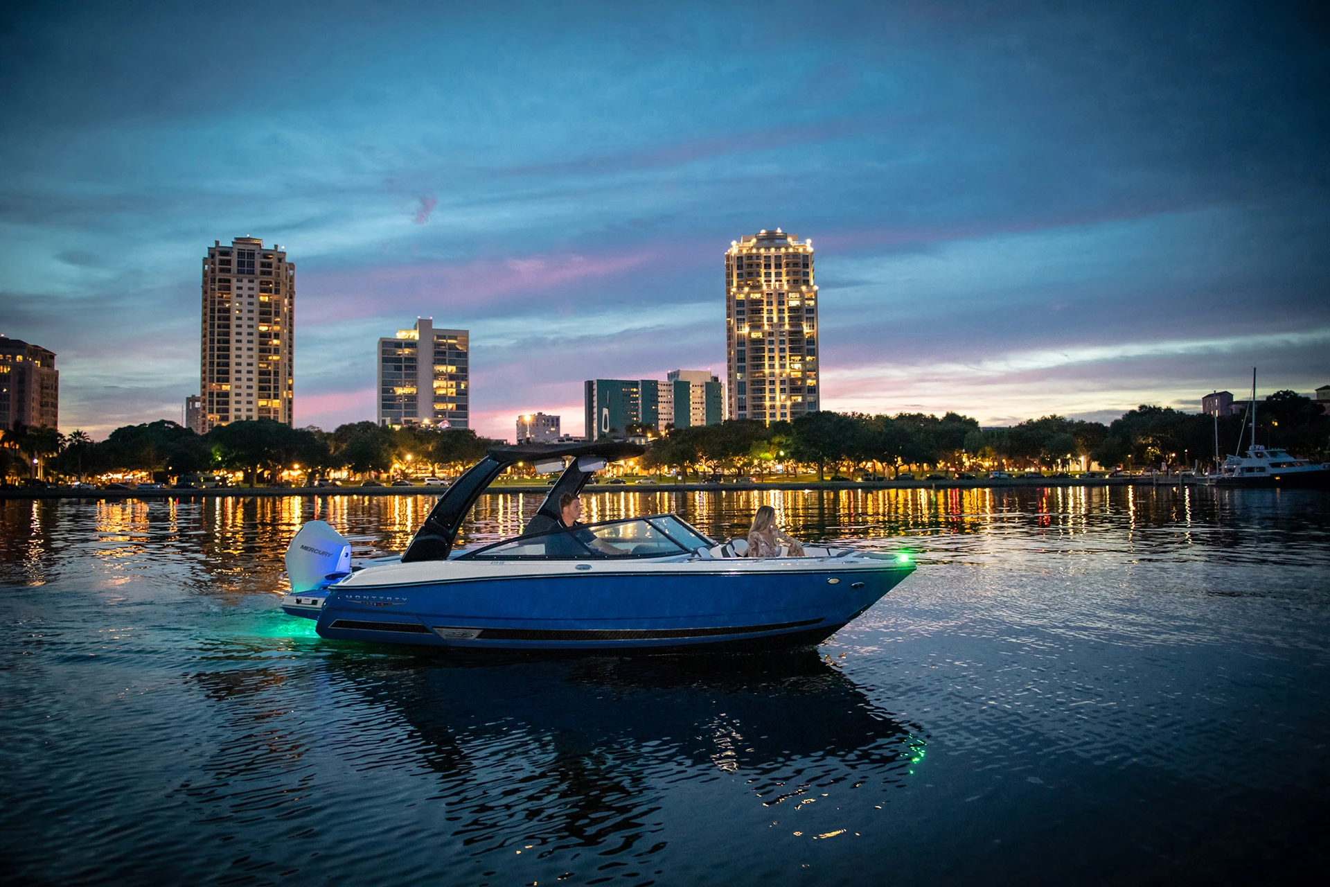 Monterey 235SS illuminated with underwater lights, cruising near a city skyline at dusk