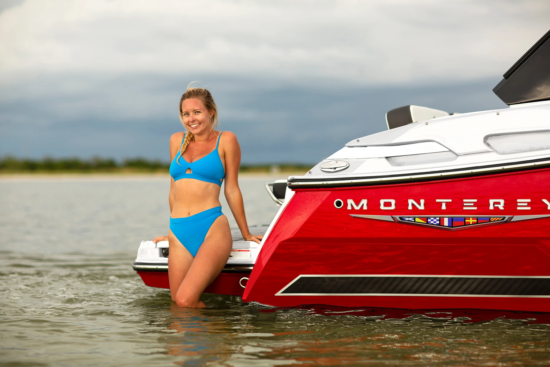 Person standing in shallow water beside the red Monterey 258SS transom with “MONTEREY” badge visible