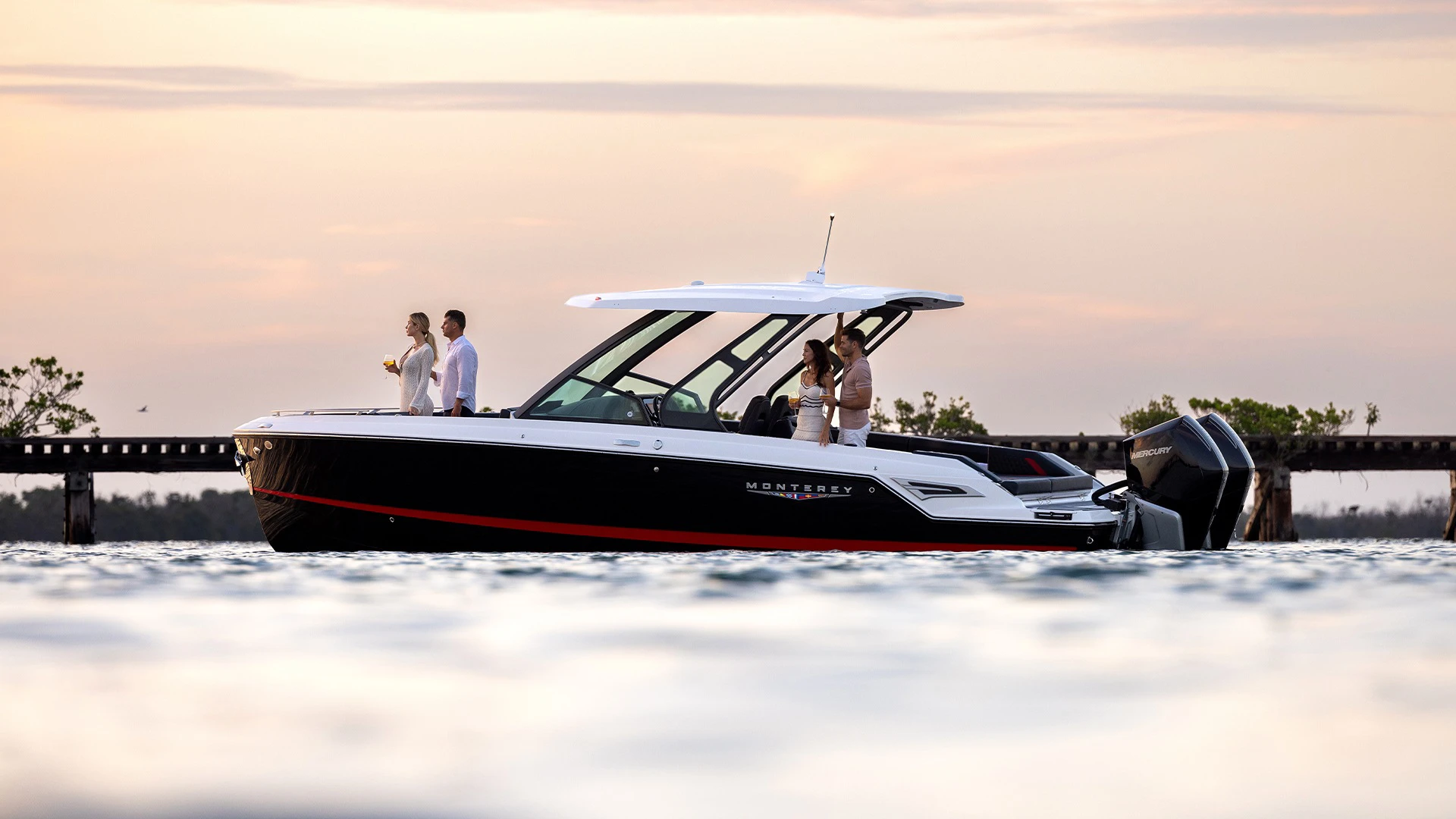 Side view of the Monterey Elite 30 OB cruising at sunset with passengers enjoying drinks on deck