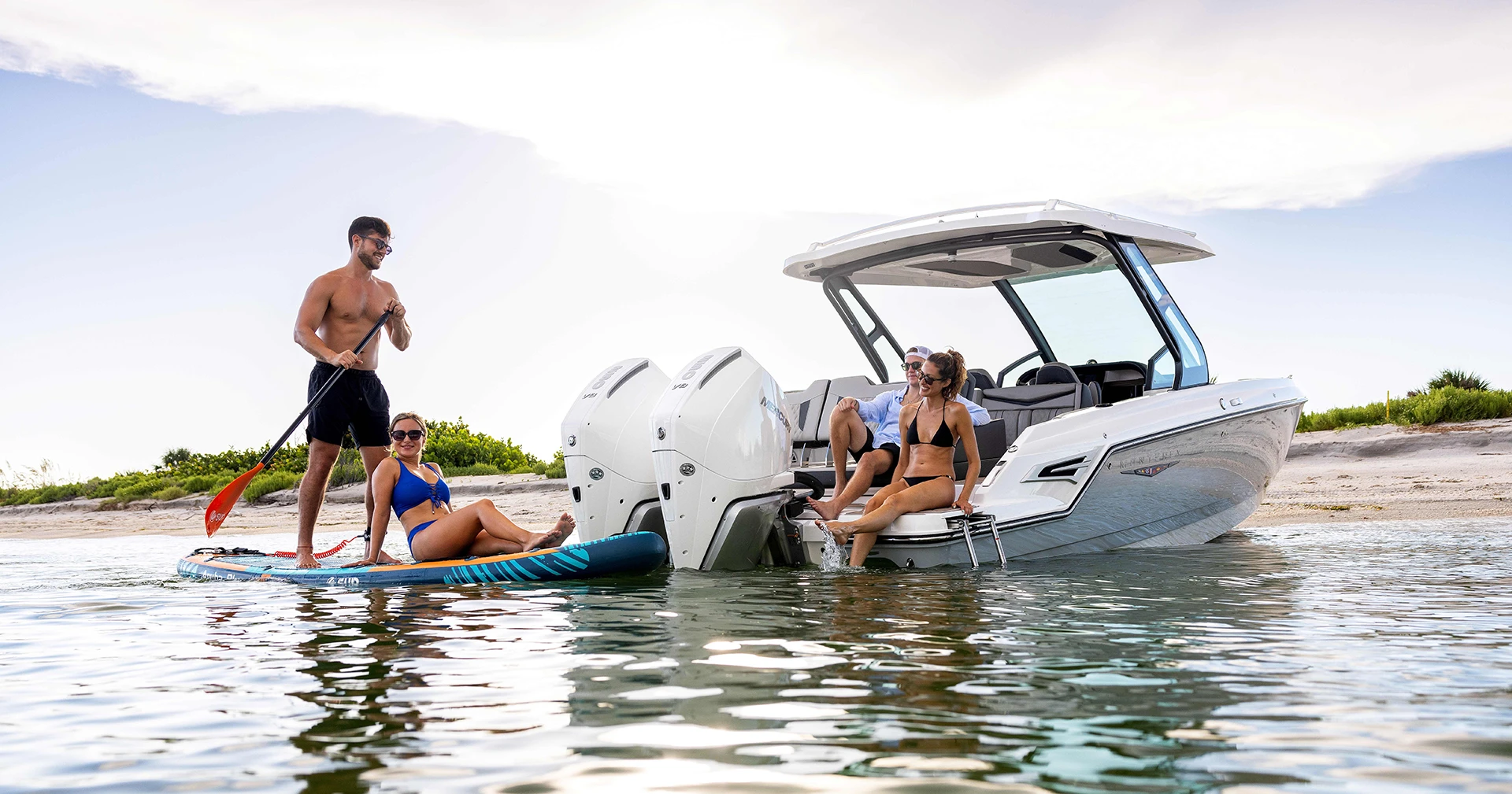 Elite 30 OB at the beach, showcasing dual Mercury outboards, extended swim platform, and lounging passengers enjoying the water