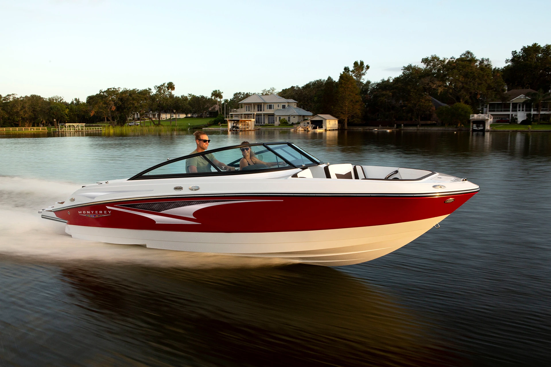 Monterey M-22 runabout in red and white cruising at speed on calm water near waterfront homes